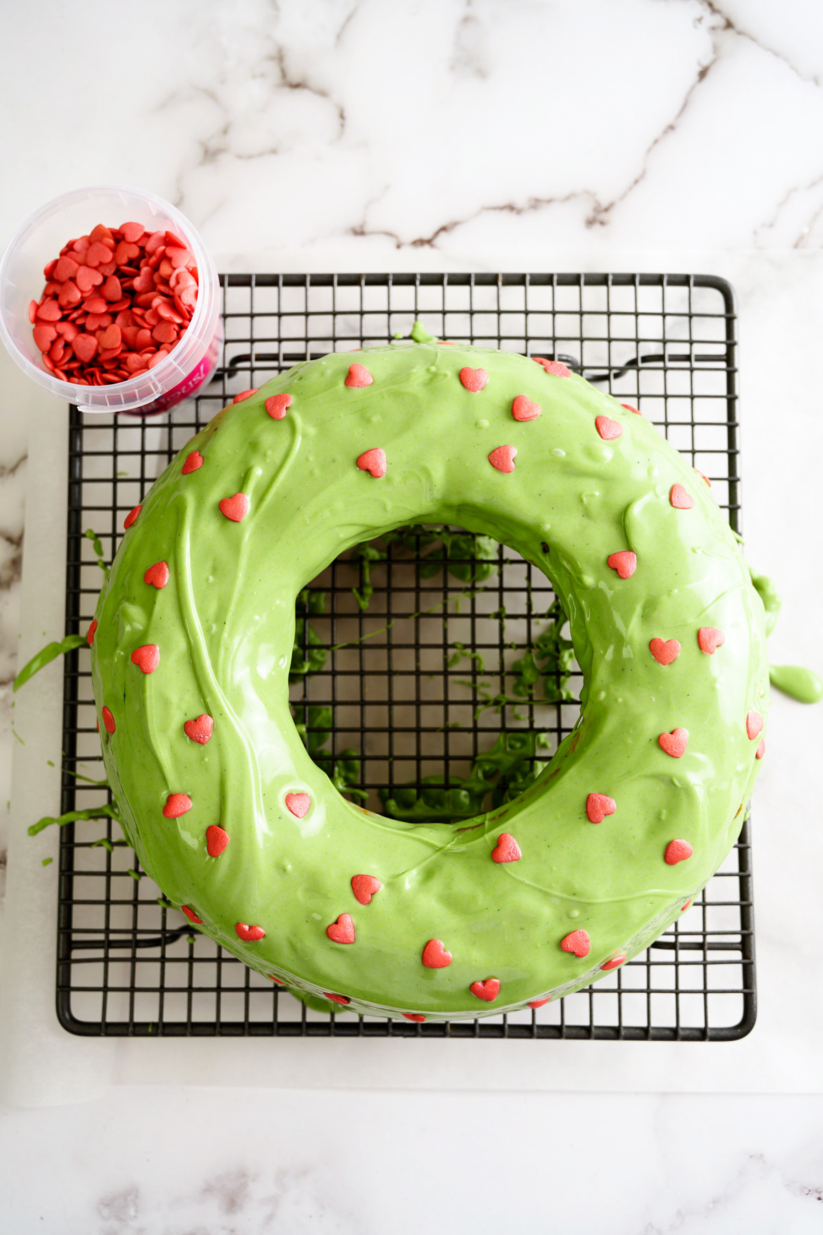 A round cake made from a banana cake recipe, coated in green icing and decorated with heart sprinkles.