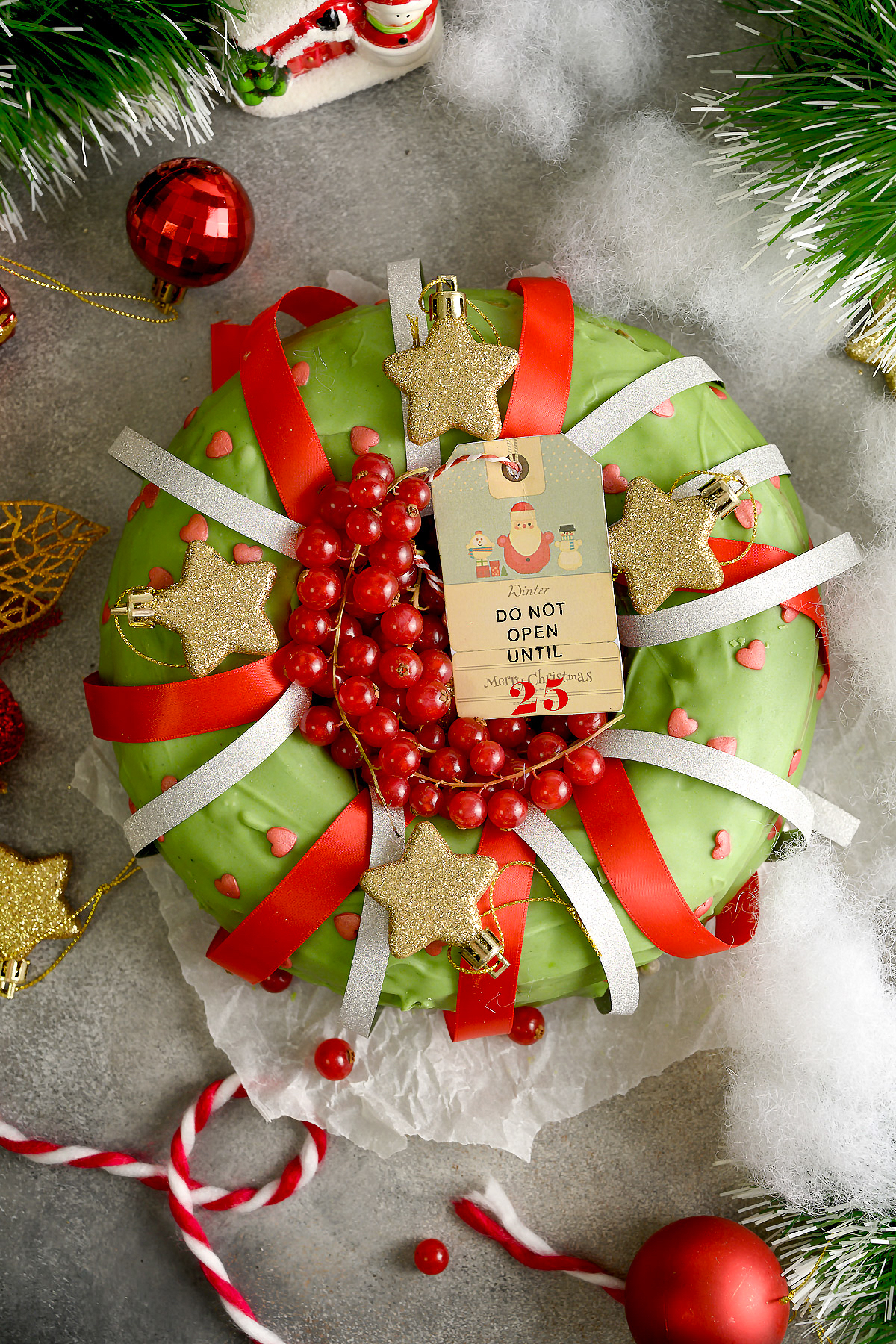 A Christmas banana cake decorated with green frosting, ribbons, sprinkles, and more.