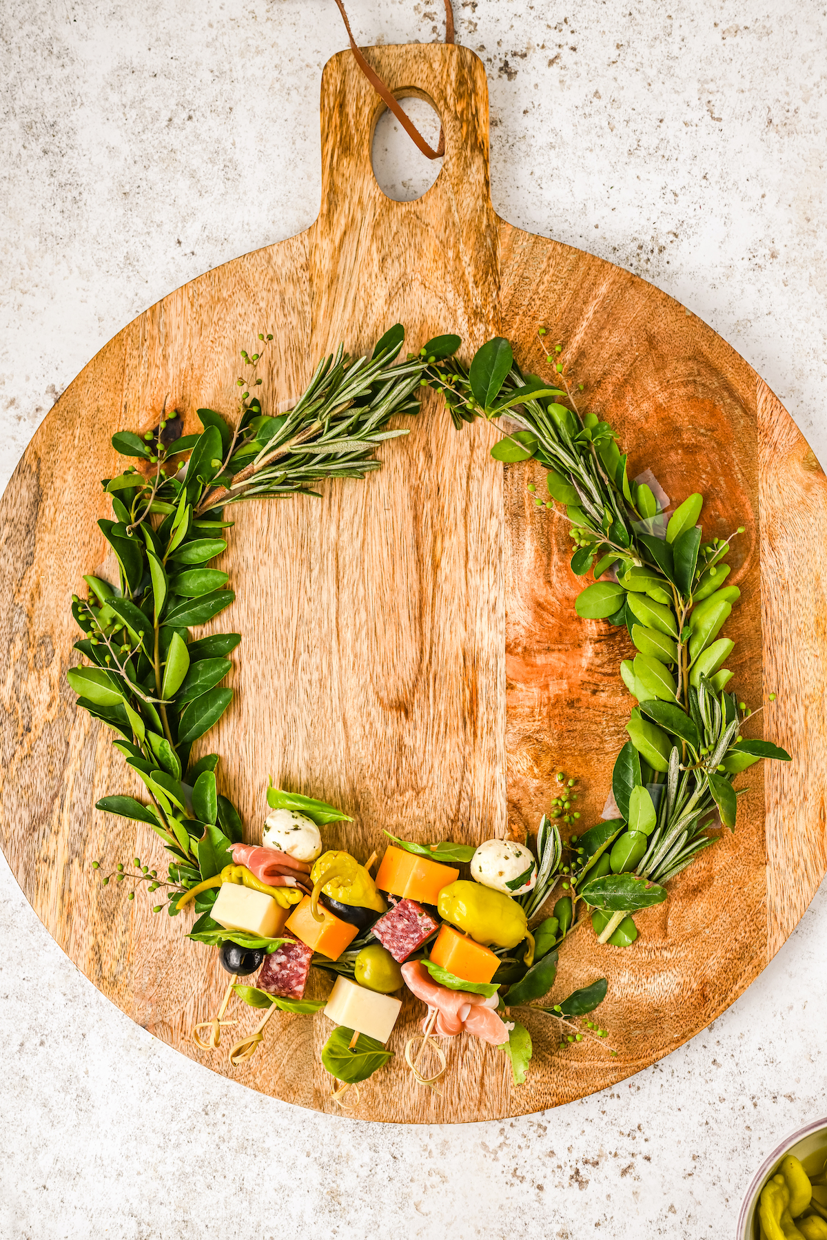 Small skewers of antipasto arranged on a circle of greenery on a cutting board.