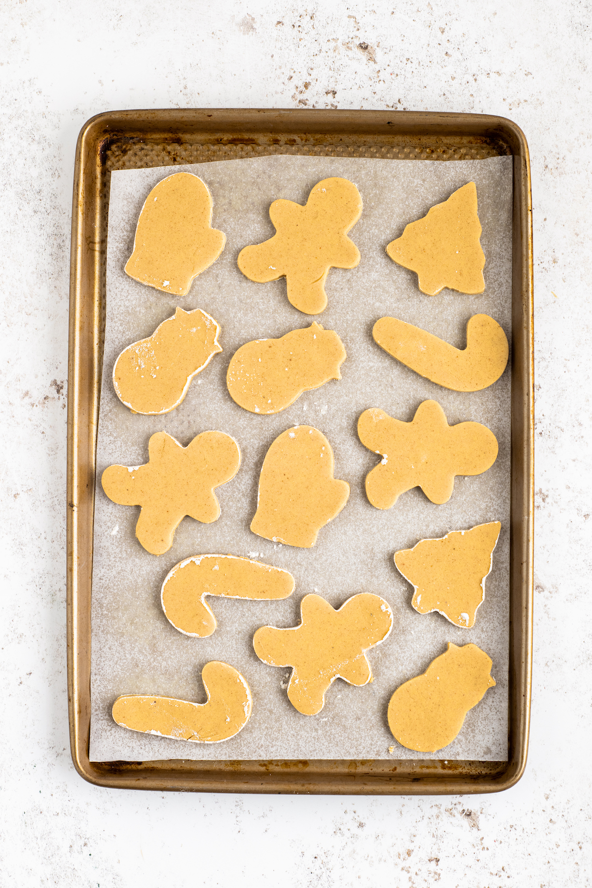 A cookie sheet lined with parchment, and cut-out unbaked cookies on it.