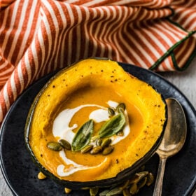 Creamy fall soup in an acorn squash bowl topped with pumpkin seeds and sage.