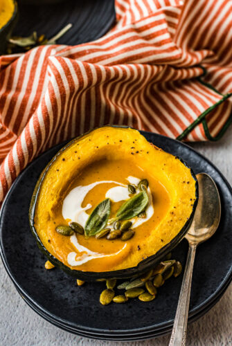 Creamy fall soup in an acorn squash bowl topped with pumpkin seeds and sage.
