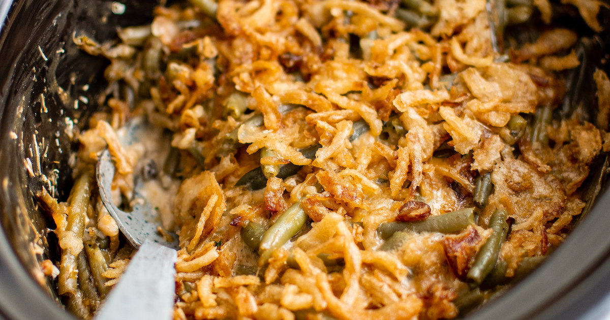 Crockpot green bean casserole with fried onions on top and a spoon inside.