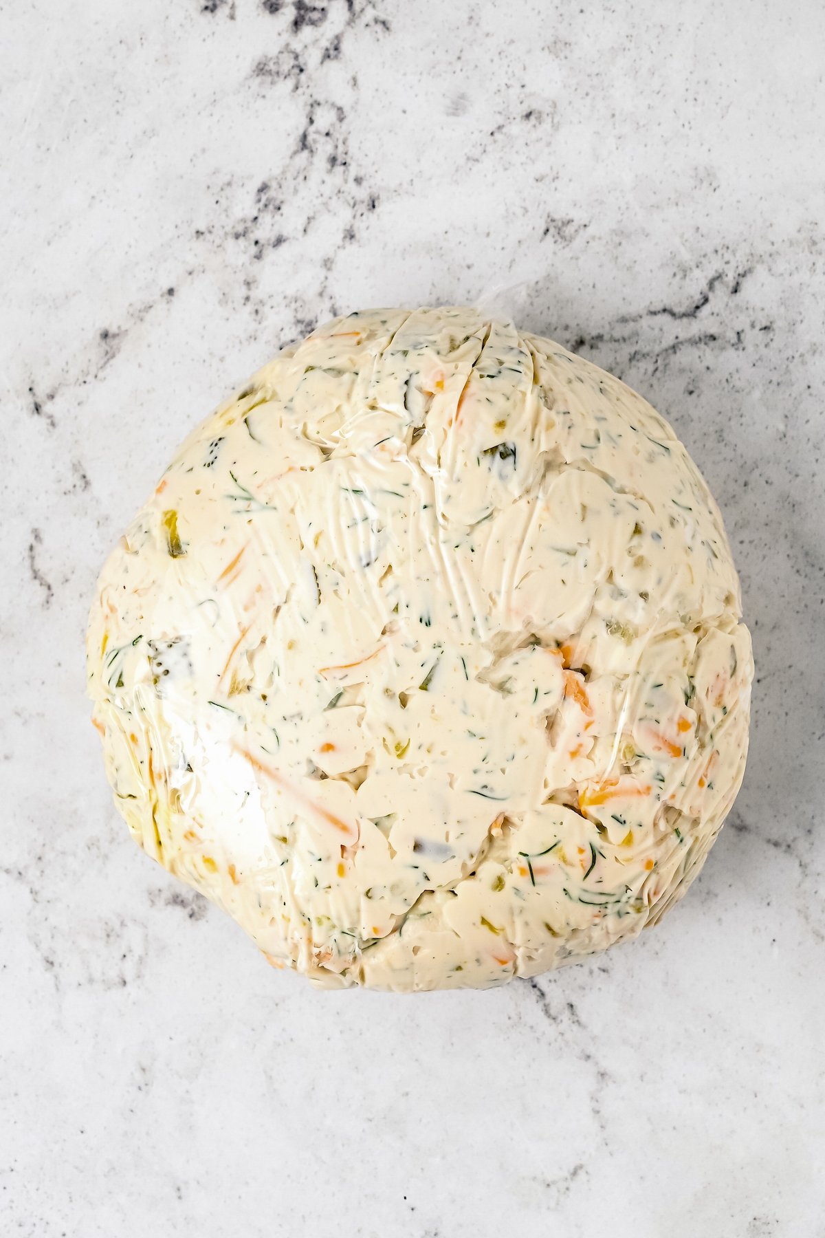 A cheese ball mixture tied up in plastic wrap.