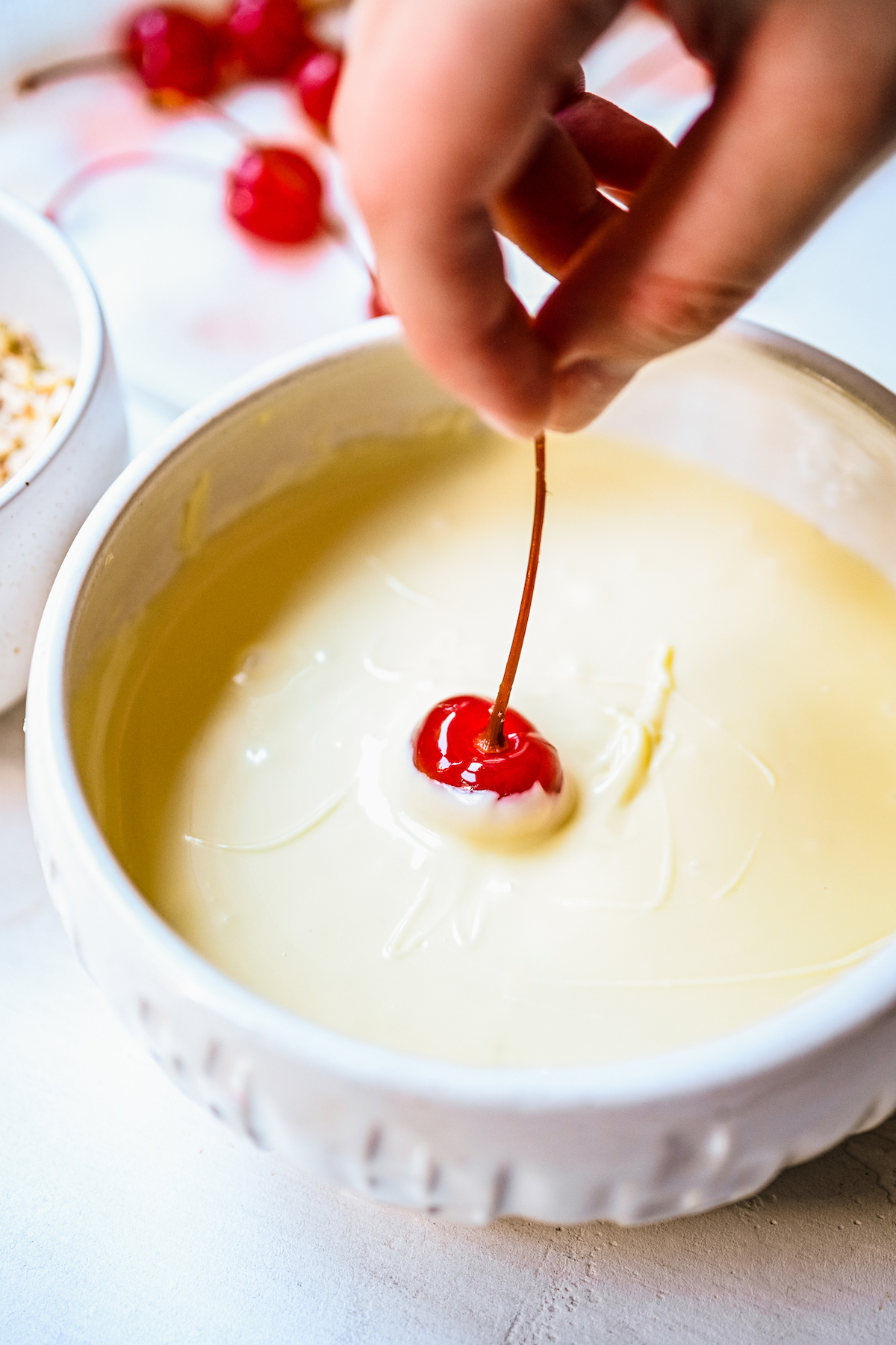 A cherry being dipped in melted white chocolate.