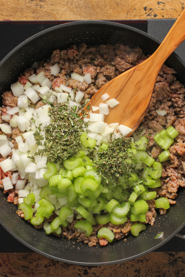 Sausage, onion, celery, herbs, and other ingredients cooking in a skillet.