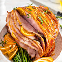 A spiral-sliced ham with orange slices, rosemary, and glaze.