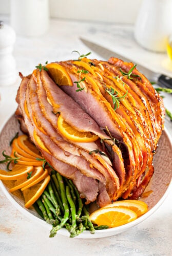 A spiral-sliced ham with orange slices, rosemary, and glaze.