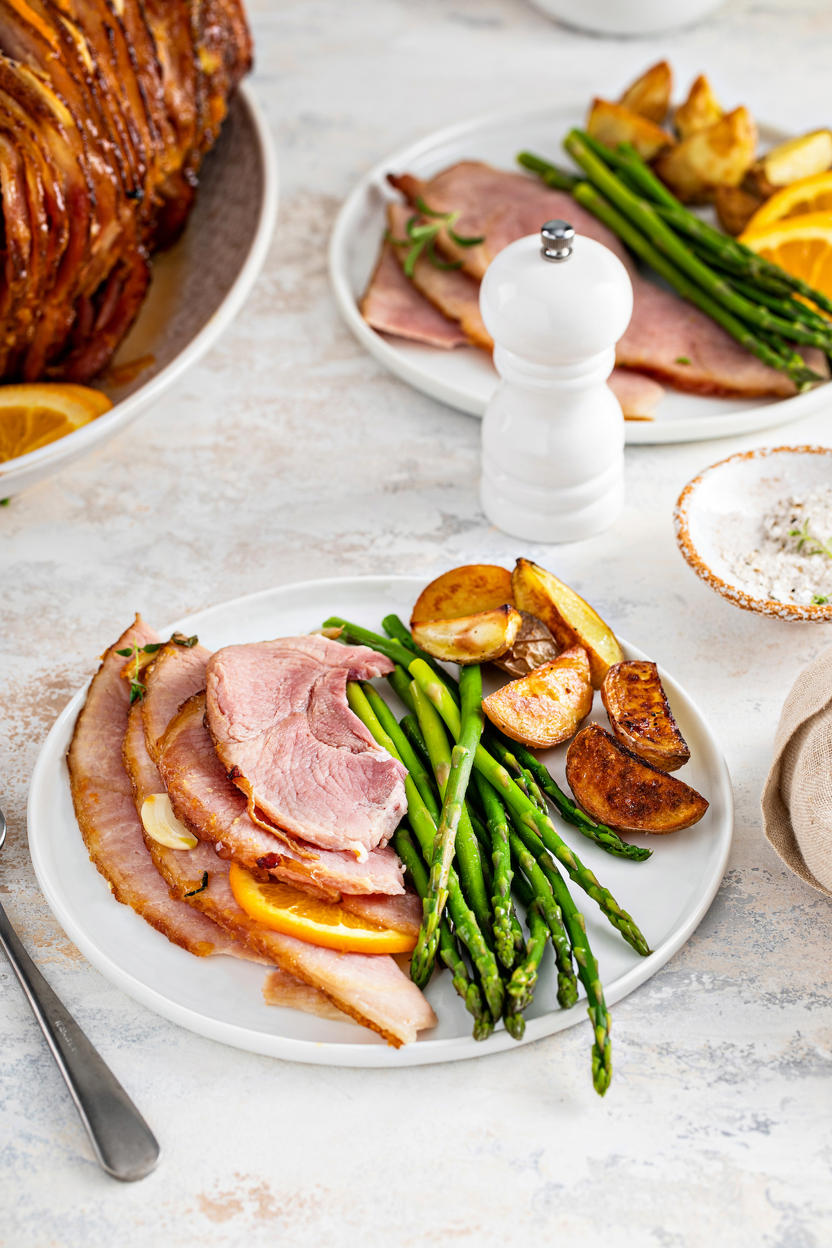 A dinner plate served with ham slices, asparagus, and potatoes.