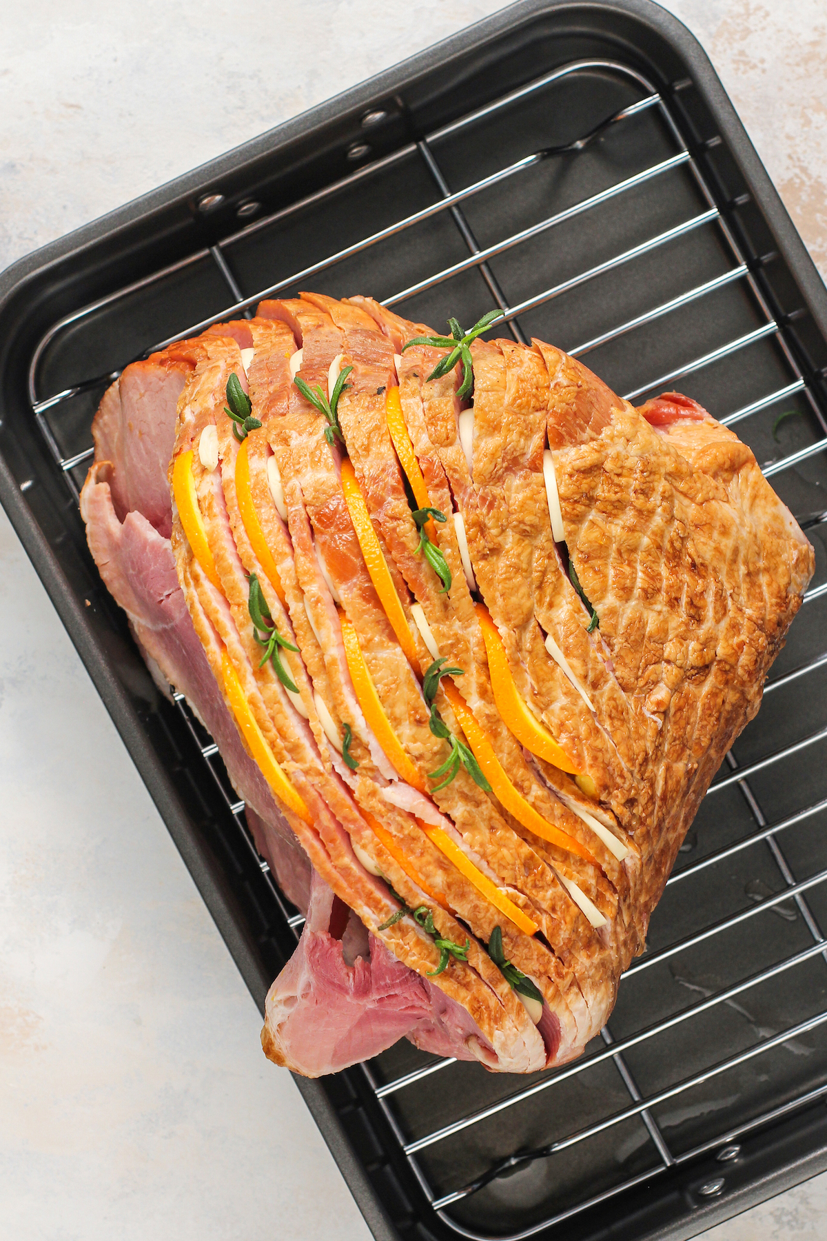 A ham with herbs and thin slices of orange tucked in between the slices.