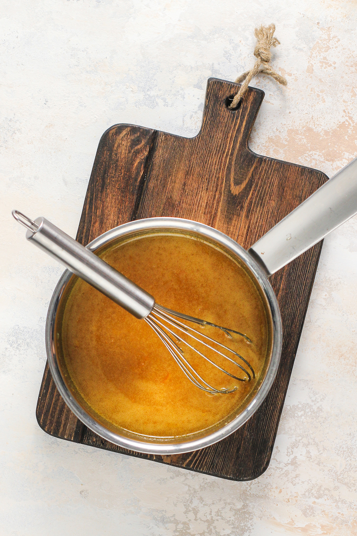 A saucepan with orange marmalade glaze and a whisk.