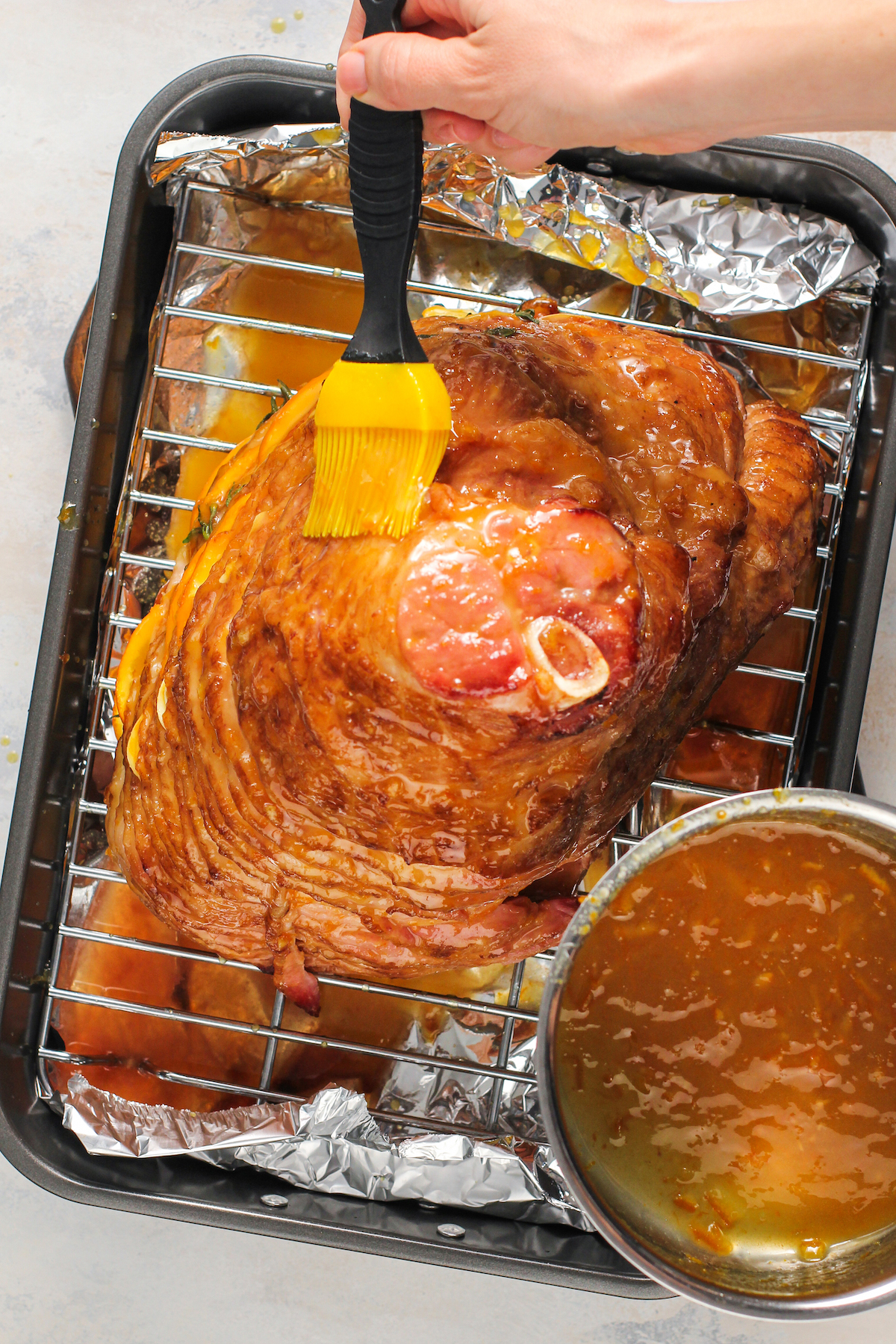 A spiral ham on a roasting rack, being brushed with glaze.