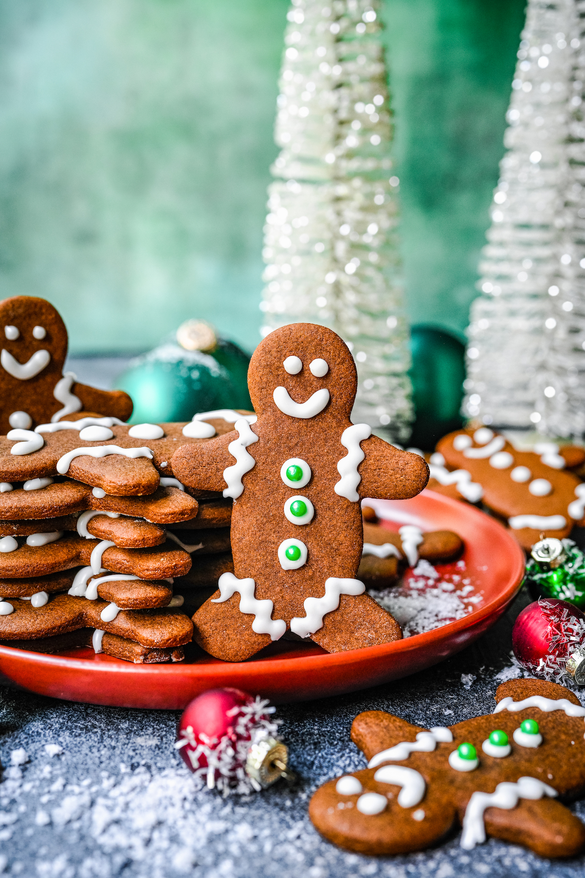A plate of gingerbread cookies. One is standing up against a stack of other cookies, showing the royal icing details.