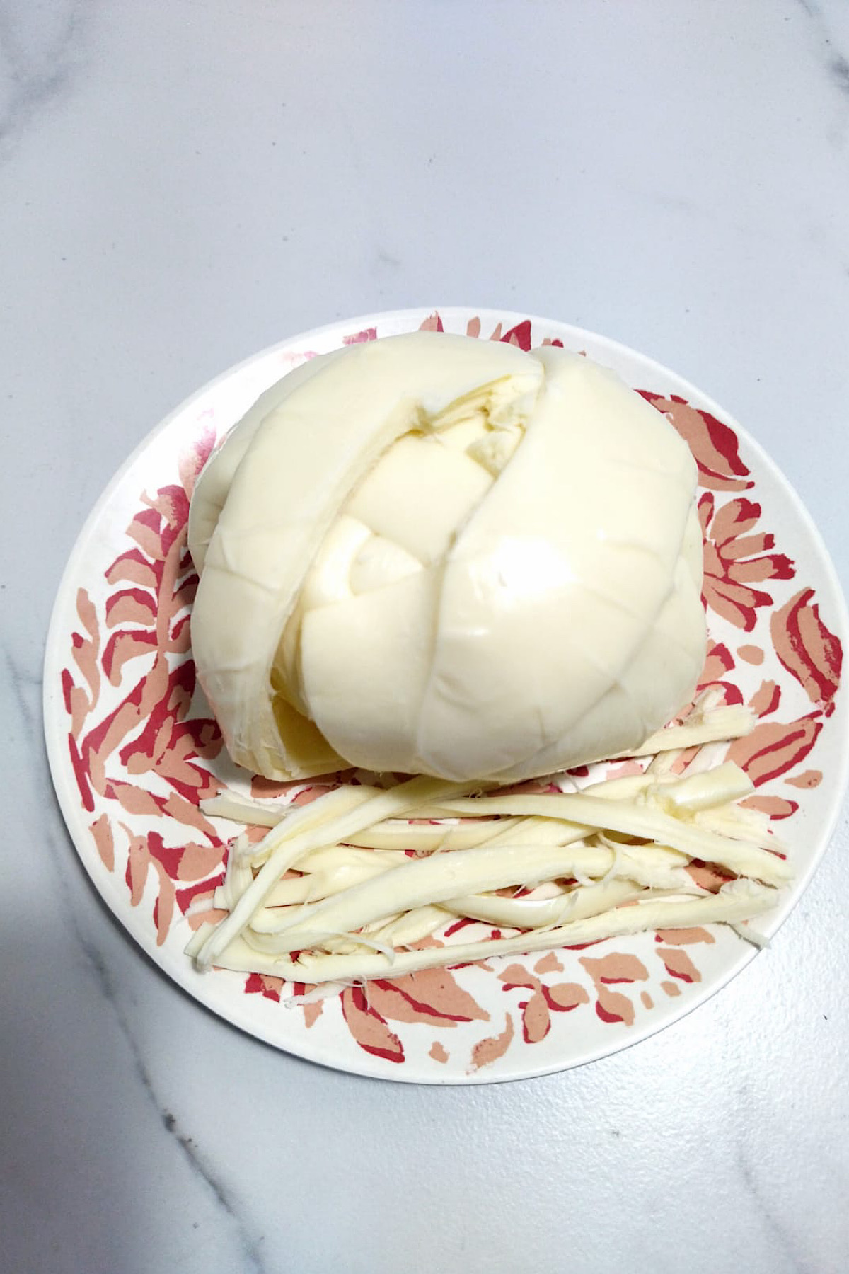 Ball of oaxaca cheese with shredded cheese on the side. 