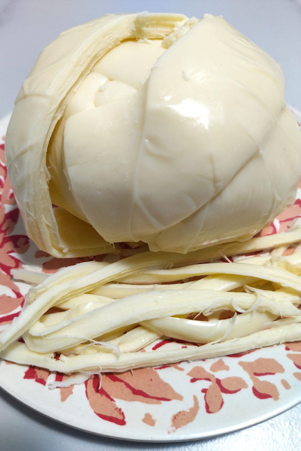 Close up of oaxaca cheese with shredded bits on the side.