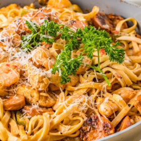 A large cooking pot of creamy pasta with shrimp, chicken, and sausage.