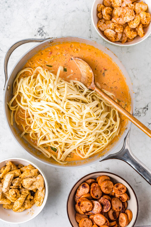 Featuring chicken, sausage, and shrimp, this creamy Cajun Pasta recipe is tossed in a creamy and spicy sauce with tender linguine pasta. Cooked pasta being stirred into Cajun sauce.