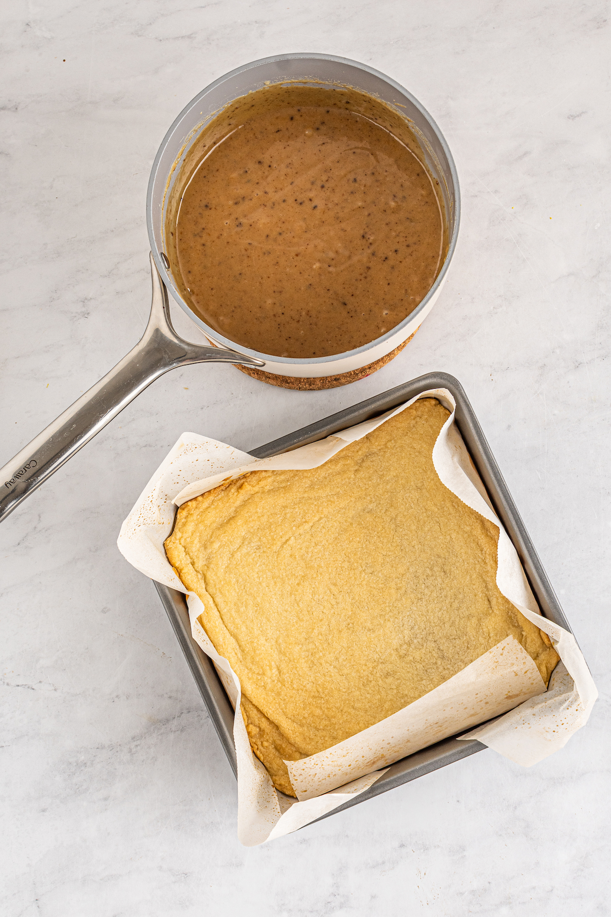 A pot of caramel sauce next to a baking pan with shortbread in the bottom.