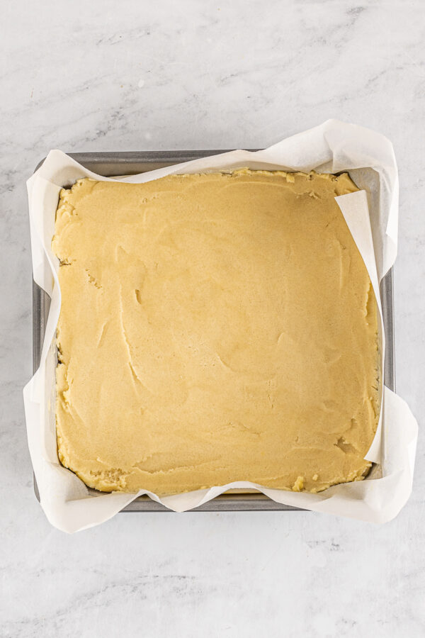 Shortbread dough spread into a square baking dish lined with parchment.