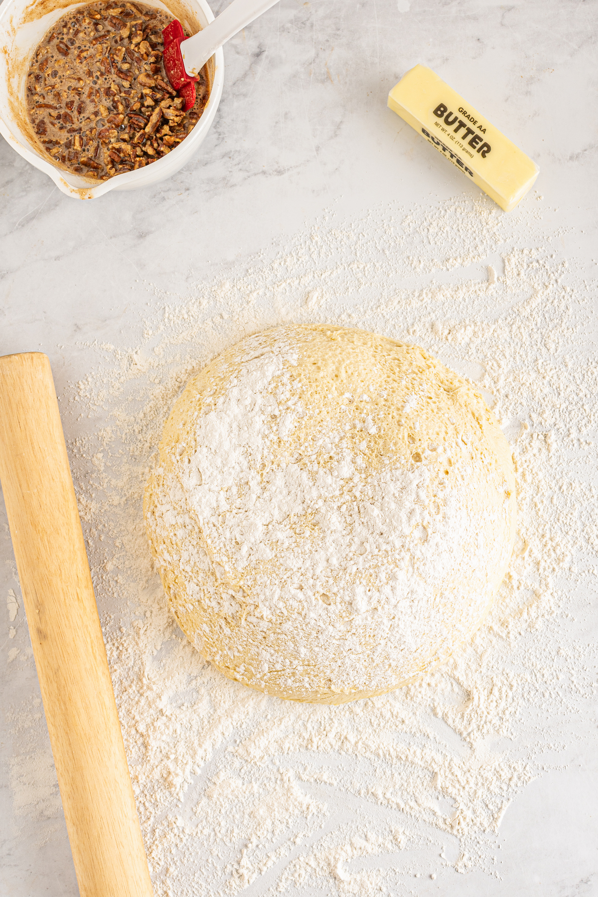 Dough turned out onto a floured surface next to a rolling pin, a container of filling, and a stick of softened butter.