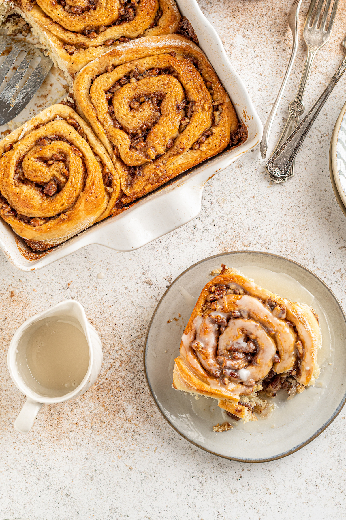 Overhead shot of a pan of cinnamon rolls with one on a small plate.
