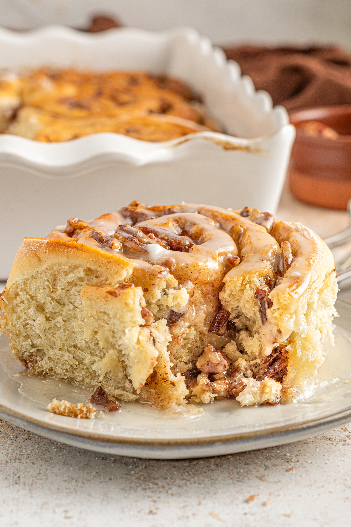 A pecan cinnamon roll on a plate in front of a baking dish.