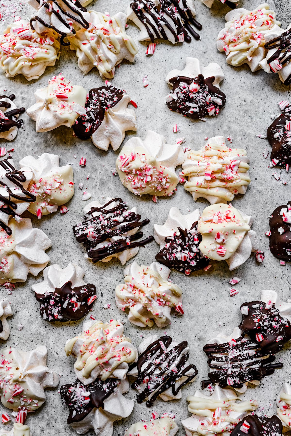Meringues on a tray. Some are dunked in semisweet chocolate, some dunked in white chocolate, and decorated with crushed candy canes.