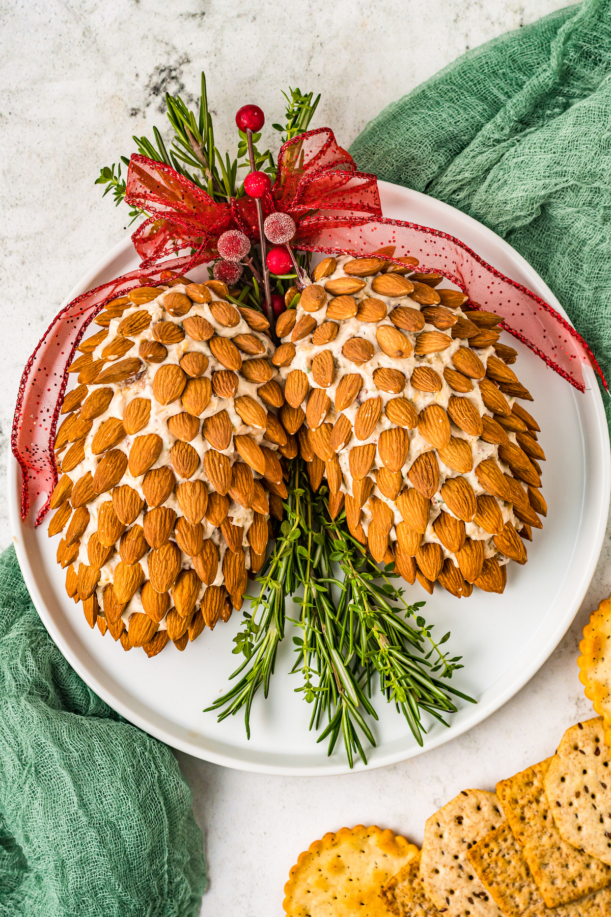 Pine cone cheese balls on a platter, garnished with herbs, ribbons, and cranberries.