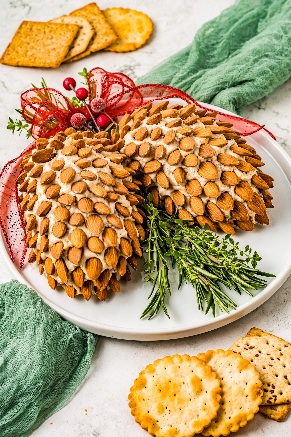 A platter with two cheese balls shaped like pinecones, with crackers and a green cloth napkin.