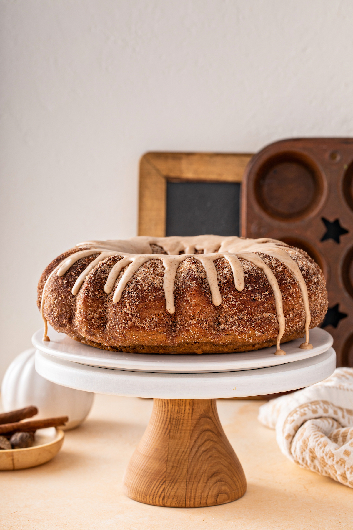 A cake stand holding a pumpkin spice bundt cake coated in cinnamon sugar and topped with glaze.