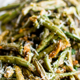 Roasted green beans on a white plate with cheese sprinkled on top.