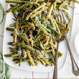 Roasted green beans on a serving tray with large serving utensils.