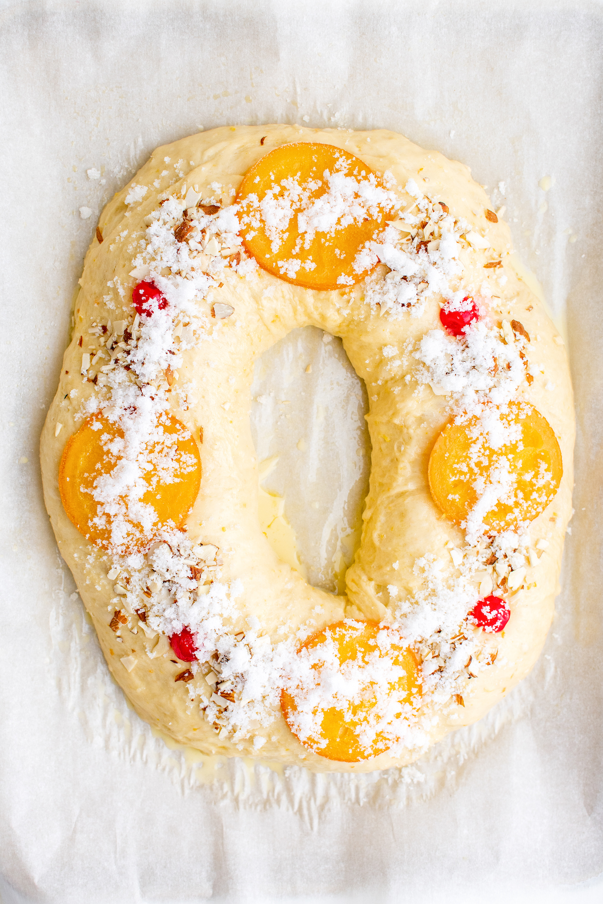 Decorating the roscón with candied oranges, cherries, and almonds. It's then sprinkled with the sugar mixture.