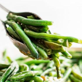 Satueed green beans being scooped up with tongs out of a skillet.