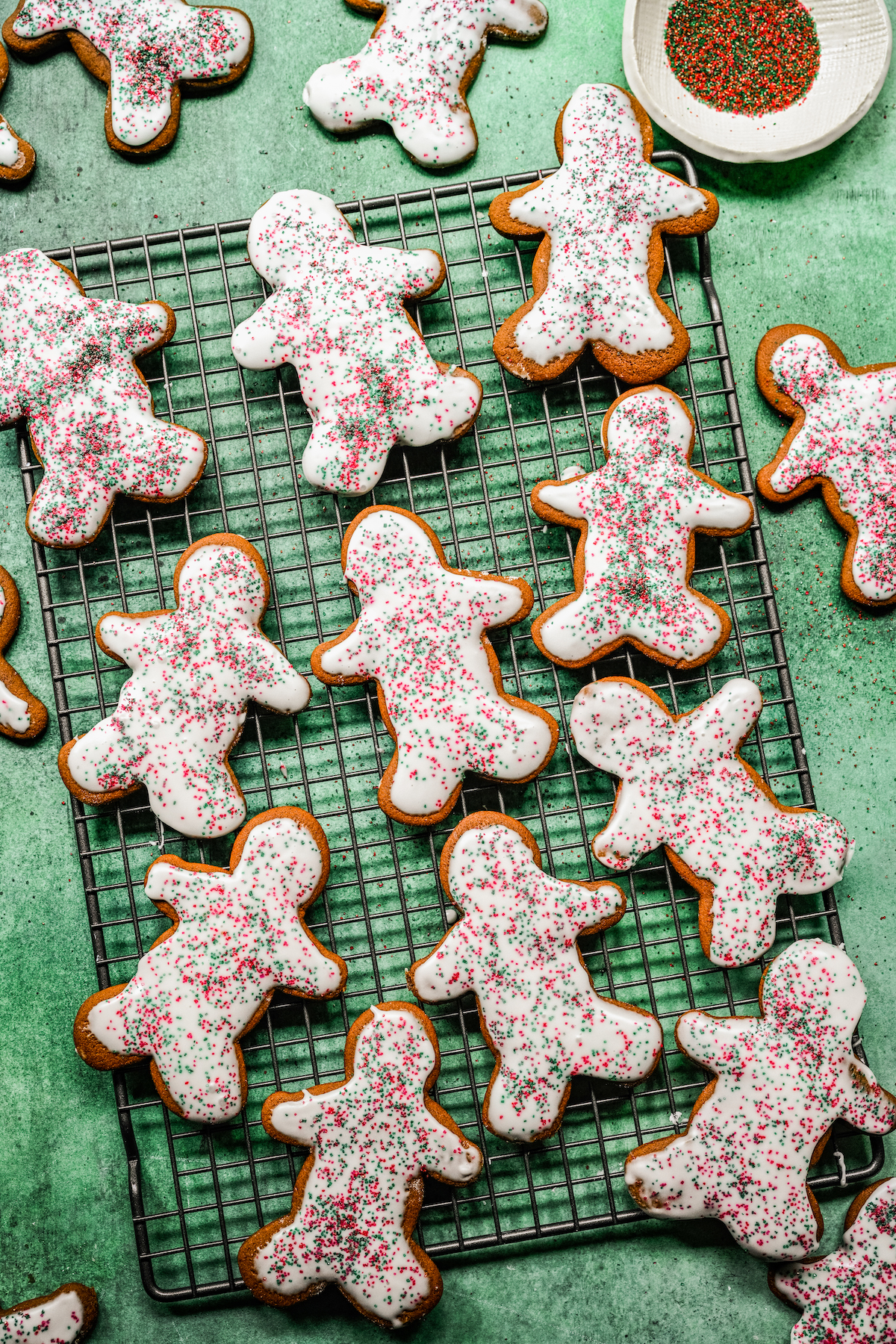 Iced gingerbread cookies on a wire rack, sprinkled with red and green sprinkles.