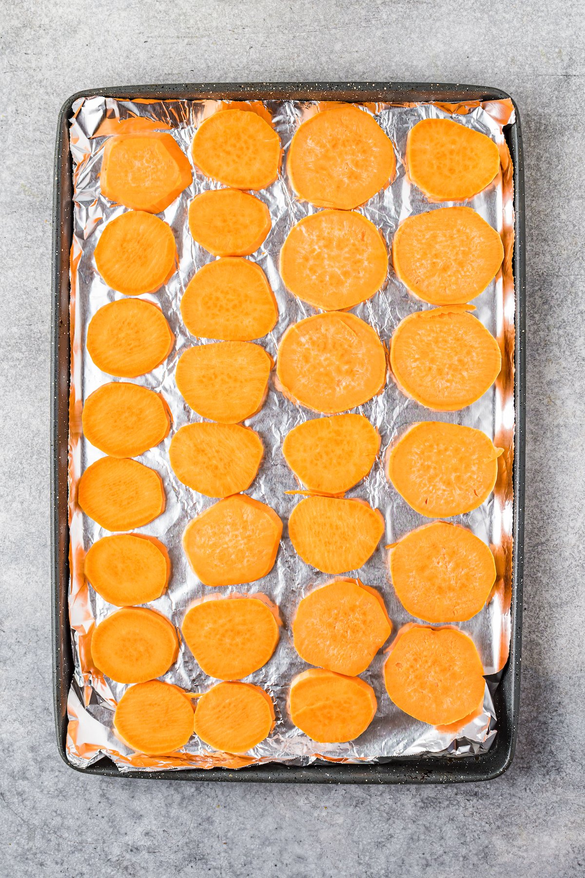 Sliced sweet potatoes on the prepared baking tray.