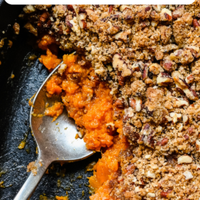 A spoon scooping out a serving of sweet potato casserole with pecan topping out of a casserole dish.