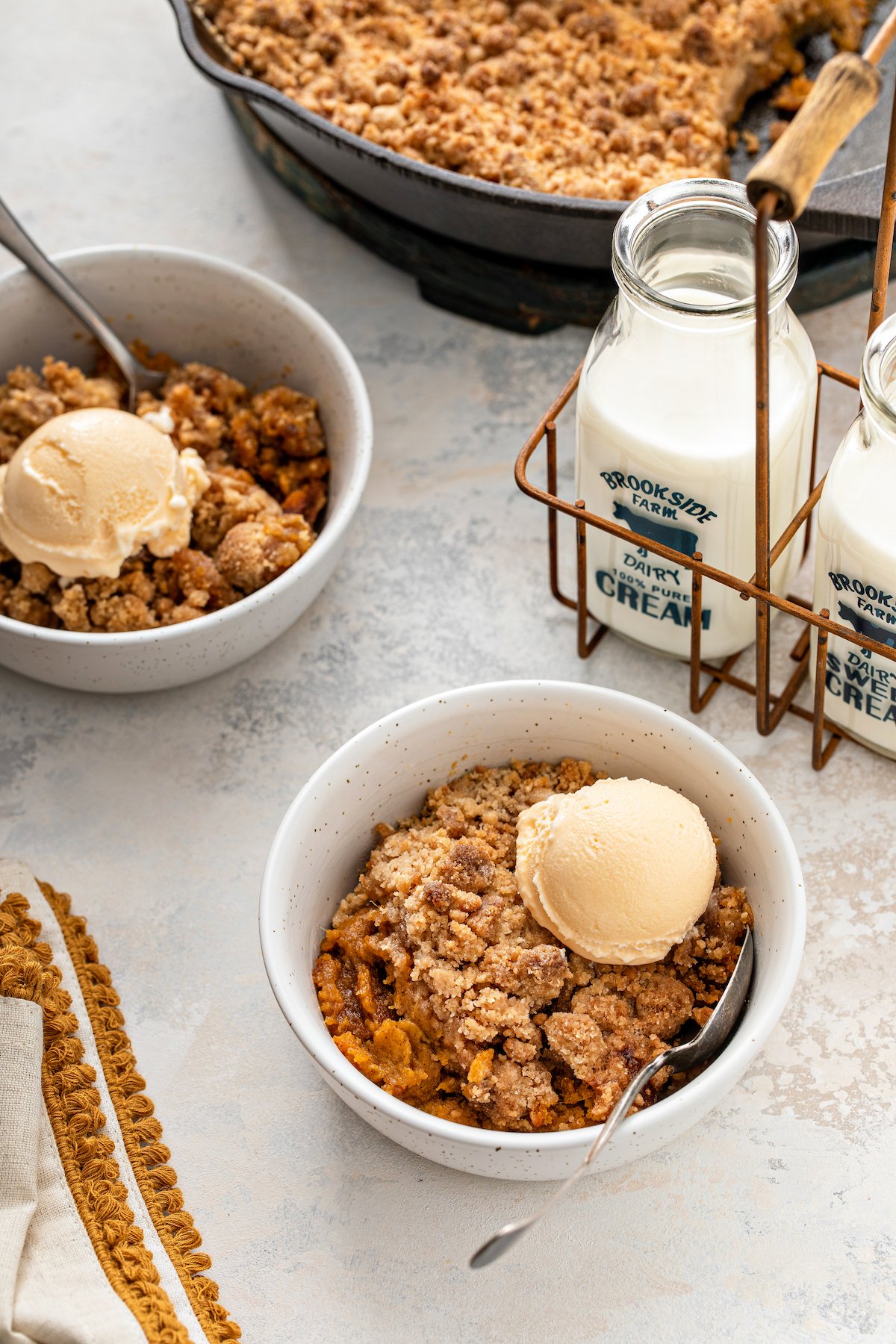 A sweet potato pie crumble in two bowls and a cast iron skillet with ice cream on top of each serving.