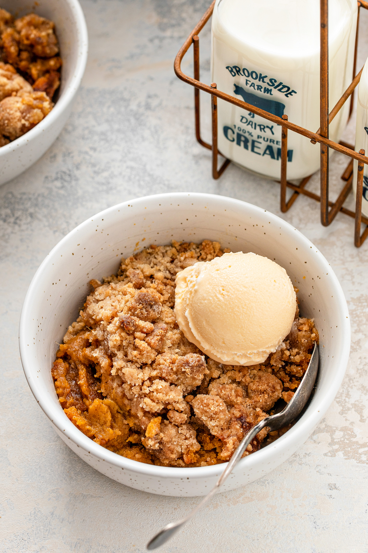 A bowl of sweet potato crumble with ice cream on top and a spoon in it.