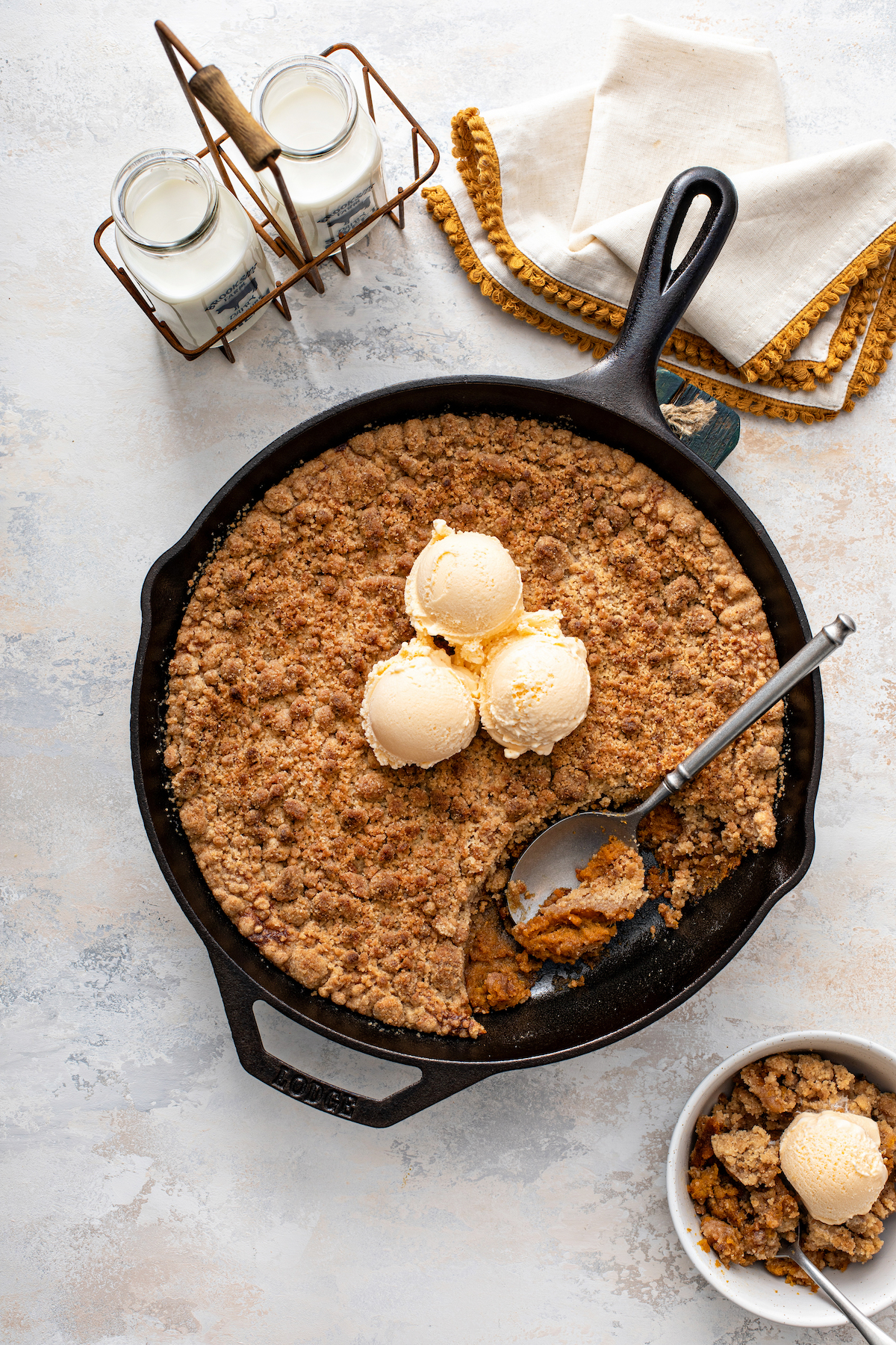 Sweet potato pie crumble in a cast iron skillet with a bowl filled with a serving.