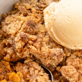 Sweet potato crumble in a bowl with ice cream on top and a spoon.
