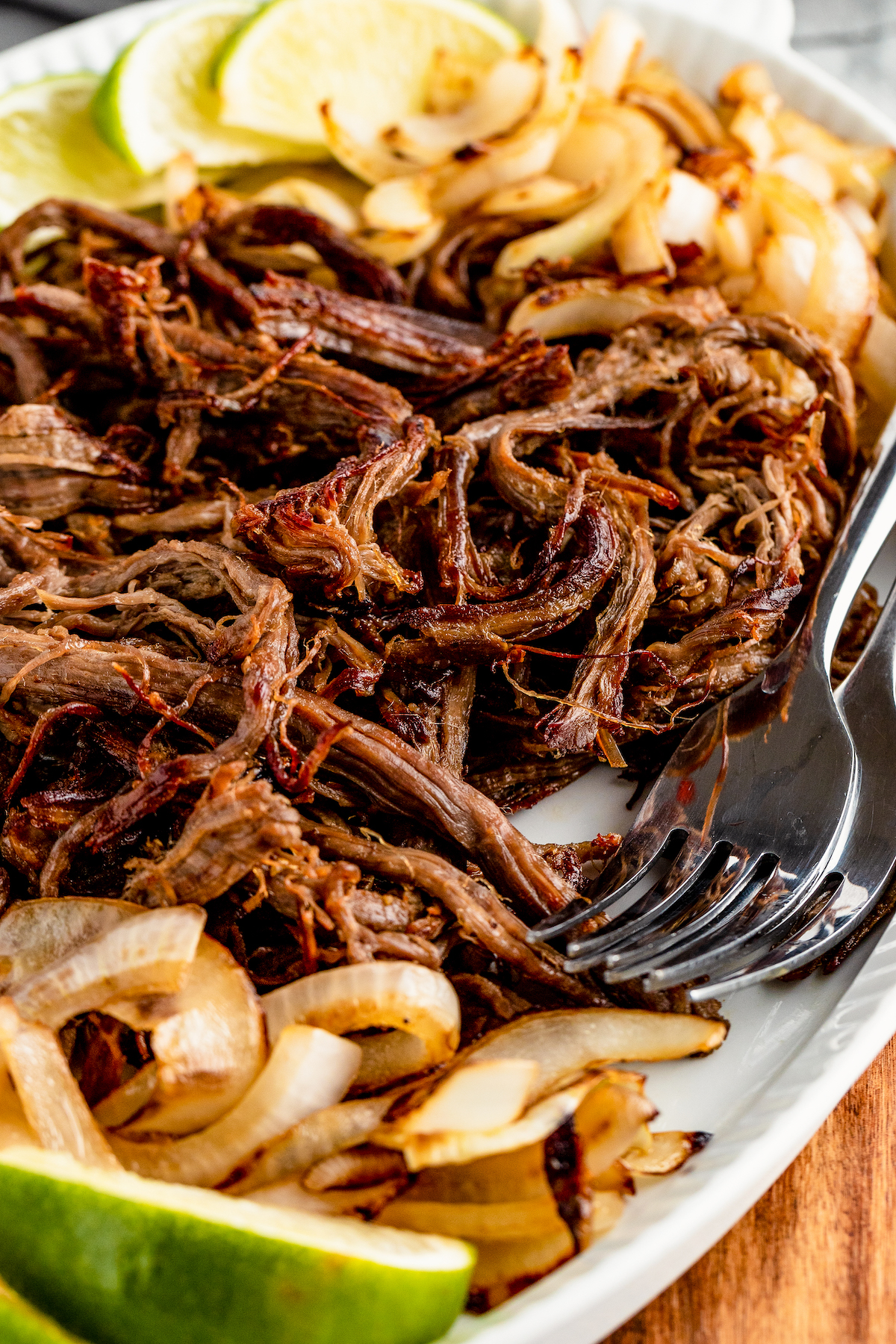 Shredded crispy beef with onions on a platter with two forks.