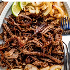 Crispy shredded cuban beef in a serving dish with onions and lime wedges.