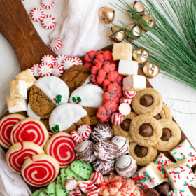 Christmas cookies and candies on a wood tray with jingle bells and peppermints.