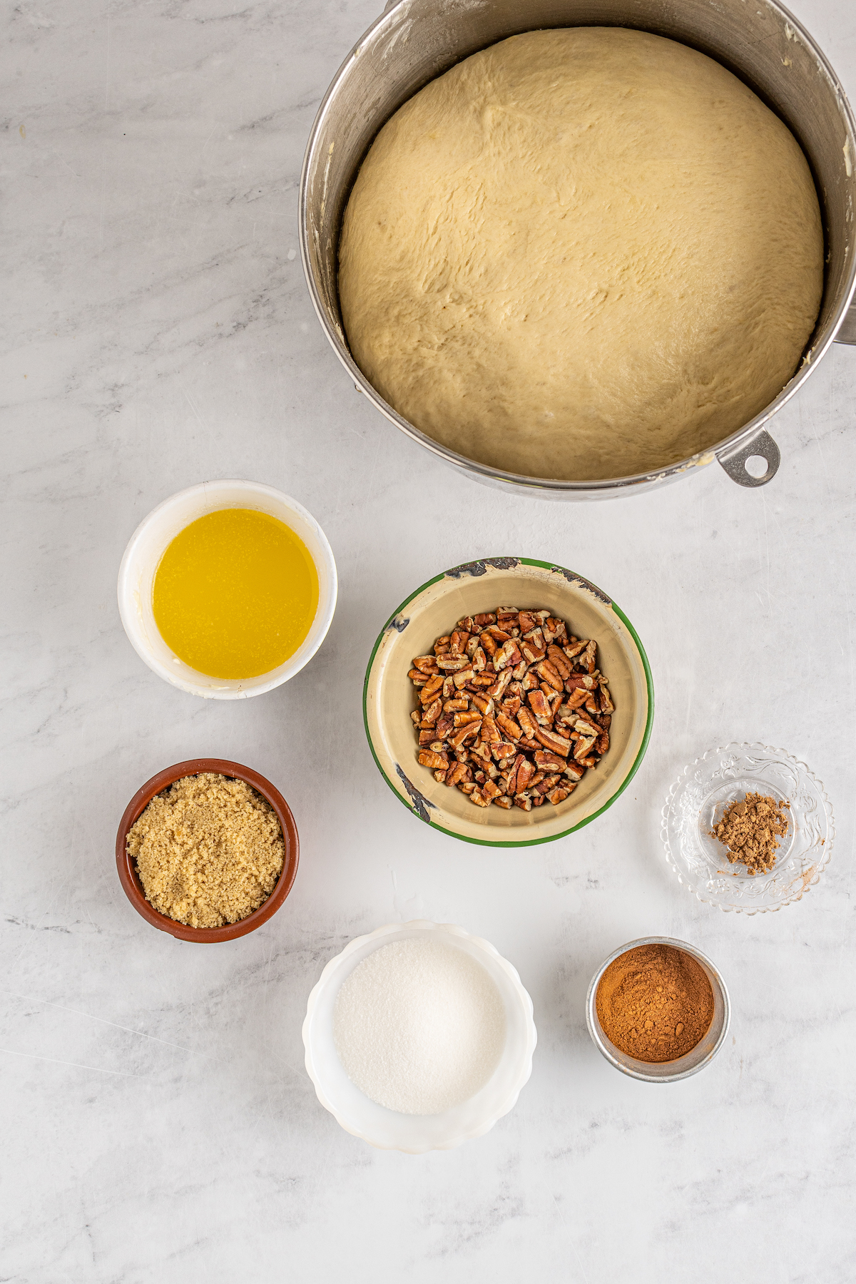 From top: A bowl of risen yeast dough, melted butter, chopped pecans, brown sugar, spices, white sugar.