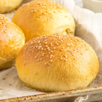 Homemade hamburger buns on a baking sheet.
