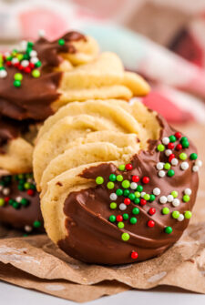 A danish butter cookie dipped in chocolate with Christmas sprinkles on parchment paper.
