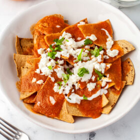 Chilaquiles rojos in a bowl with crema, cotija cheese, and cilantro.