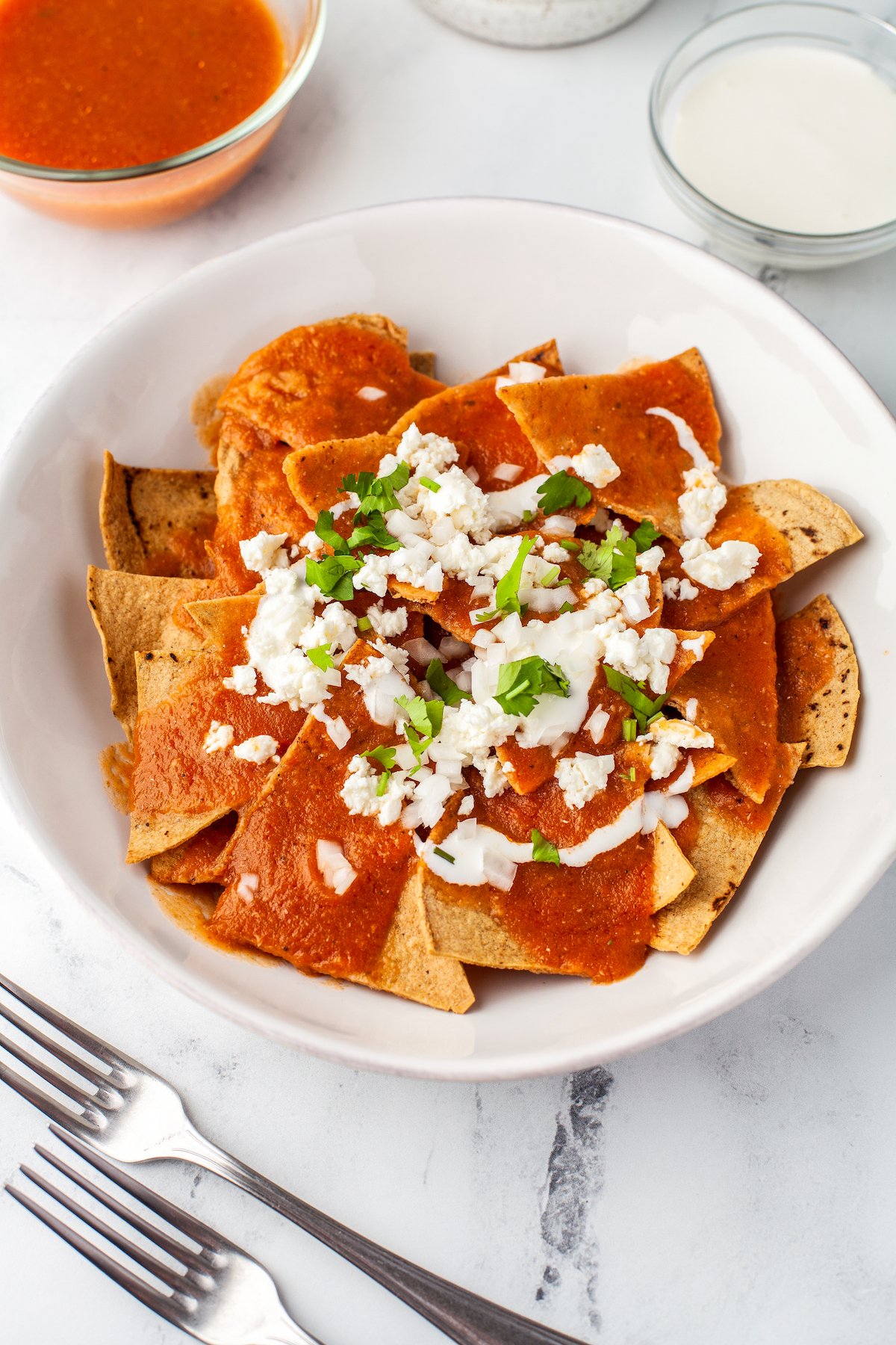 Chilaquiles rojos in a bowl with crema, cotija cheese, and cilantro.