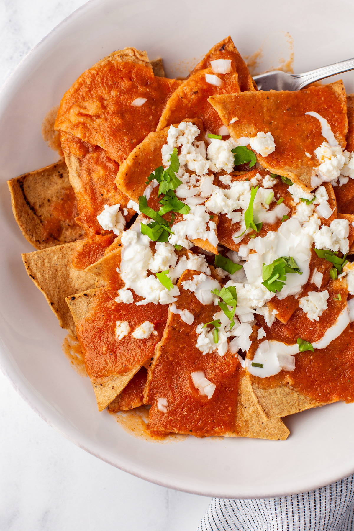 Close-up of salsa rojo spread over tortilla chips with crema, cotija cheese, and cilantro.